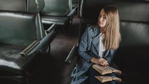 Das Bild zeigt eine Frau mit einem Buch in einem leeren Zugabteil.