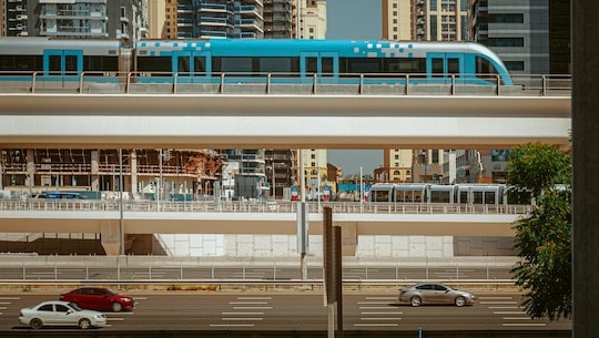 Das Bild zeigt einen Zug auf einer Brücle und Autos auf einer Straße.