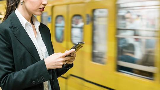 Das Bild zeigt eine Frau mit einem Smartphone vor einer vorbeifahrenden Bahn.