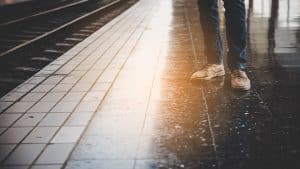 Das Bild zeigt die Beine einer Person auf einem Bahnsteig bei Regen.